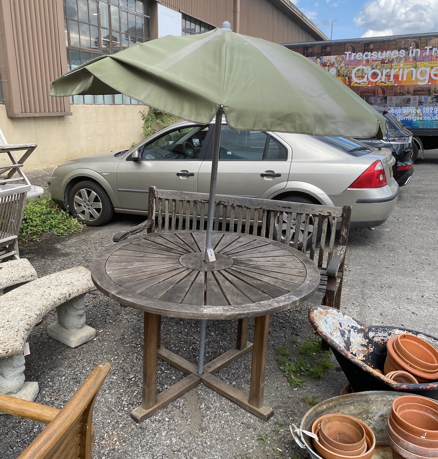 A circular weathered teak garden table, diameter 122cm, height 75cm parasol and bench